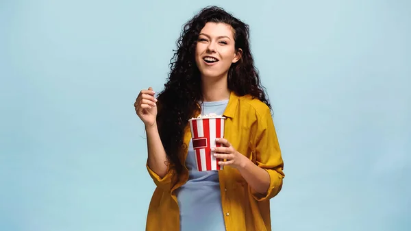 Brünette Frau mit Popcorn lacht isoliert auf blauem Grund — Stockfoto