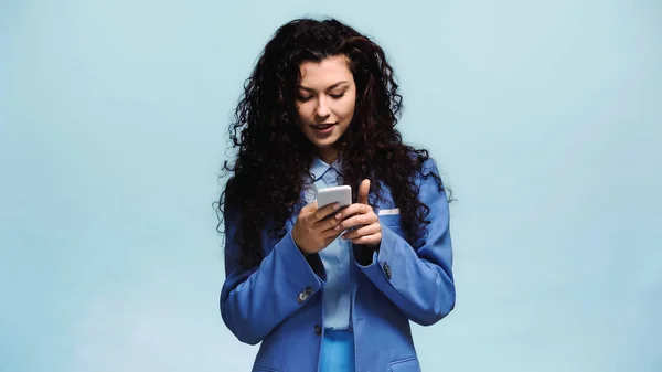 Молодая и счастливая женщина сообщения на мобильном телефоне изолированы на синий — стоковое фото