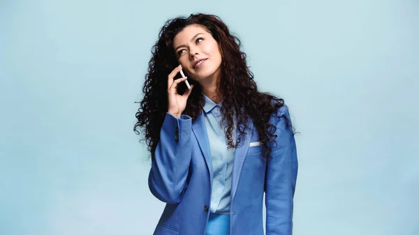 Mujer sonriente en blazer azul hablando en teléfono inteligente aislado en azul - foto de stock