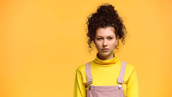 Mujer joven seria con el pelo ondulado mirando a la cámara aislada en naranja - foto de stock