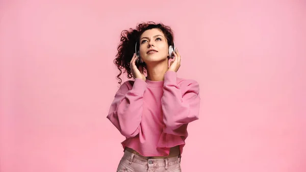 Молода жінка дивиться вгору і посміхається, слухаючи музику ізольовано на рожевому — стокове фото