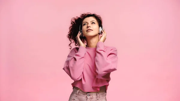 Jeune femme levant les yeux et souriant tout en écoutant de la musique isolée sur rose — Photo de stock