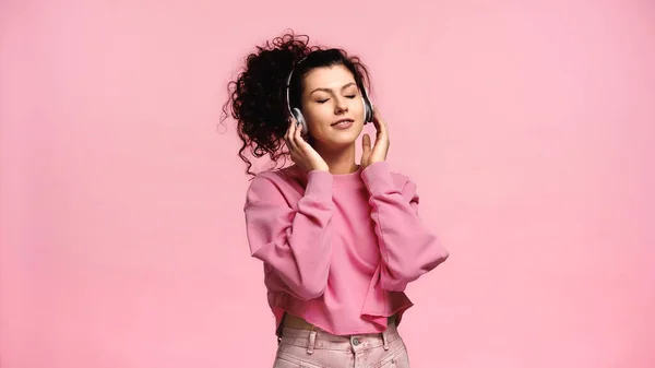 Улыбающаяся женщина слушает музыку с закрытыми глазами, изолированными на розовый — стоковое фото