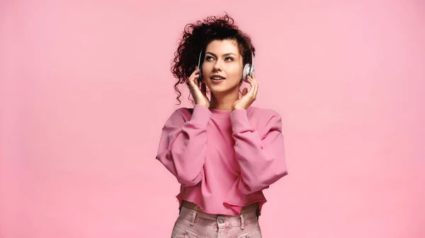 Brünette Frau genießt Musik in drahtlosen Kopfhörern isoliert auf rosa — Stockfoto