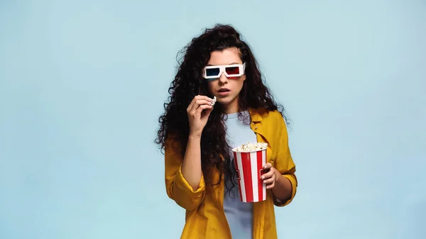 Junge Frau in orangefarbenem Hemd und 3D-Brille isst Popcorn isoliert auf blauem Grund — Stockfoto