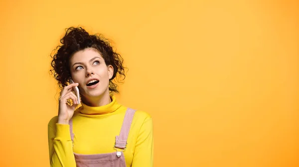 Femme surprise regardant loin pendant la conversation sur téléphone portable isolé sur orange — Photo de stock