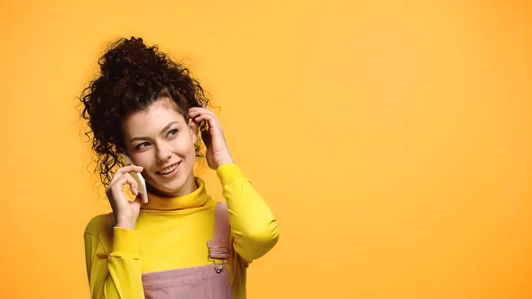 Lächelnde Frau, die während eines Gesprächs am Handy die Haare verstellt, isoliert auf Orange — Stockfoto