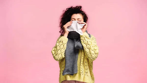 Sick woman sneezing in paper napkin with closed eyes isolated on pink — Stock Photo