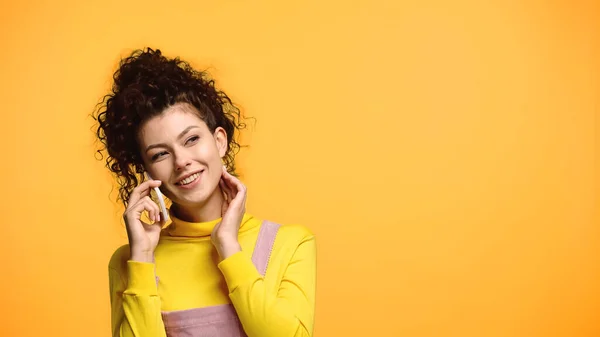 Задоволена жінка тримає руку біля шиї, розмовляючи на мобільному телефоні ізольовано на помаранчевому — стокове фото
