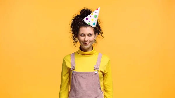 Pleased woman in yellow turtleneck and party cap looking at camera isolated on orange — Stock Photo