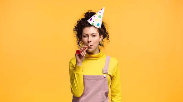 Cheerful woman in yellow turtleneck blowing in party horn isolated on orange — Stock Photo