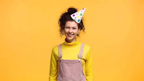 Femme gaie en chapeau de fête et col roulé jaune regardant la caméra isolée sur orange — Photo de stock