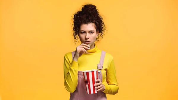 Donna concentrata in dolcevita giallo mangiare popcorn isolati su arancione — Foto stock