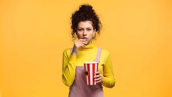 Femme inquiète avec seau de maïs soufflé regardant la caméra isolée sur orange — Photo de stock