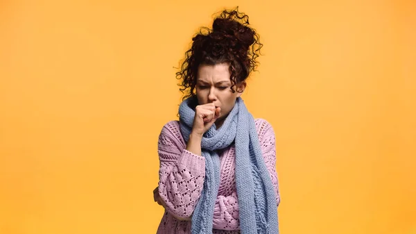 Больная женщина в теплом свитере и шарфе кашляет изолированно на оранжевом — стоковое фото
