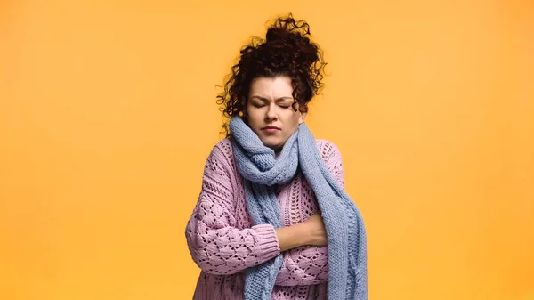 Donna congelata in maglia maglione e sciarpa in piedi con braccia incrociate isolate su arancione — Foto stock