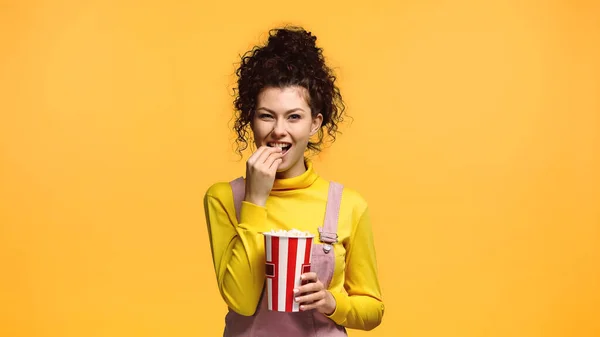 Cheerful woman with wavy hair eating popcorn isolated on orange — Stock Photo