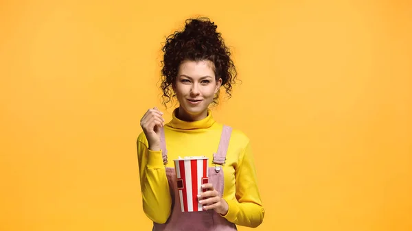 Pleased woman with curly hair eating popcorn isolated on orange — Stock Photo