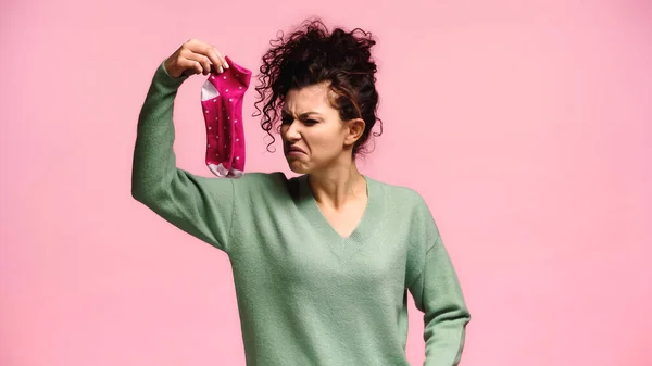 Mujer sintiéndose disgustada mientras sostiene calcetines olorosos aislados en rosa — Stock Photo