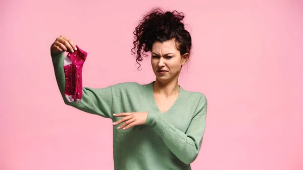 Displeased woman pointing at stinky socks and grimacing isolated on pink — Stock Photo