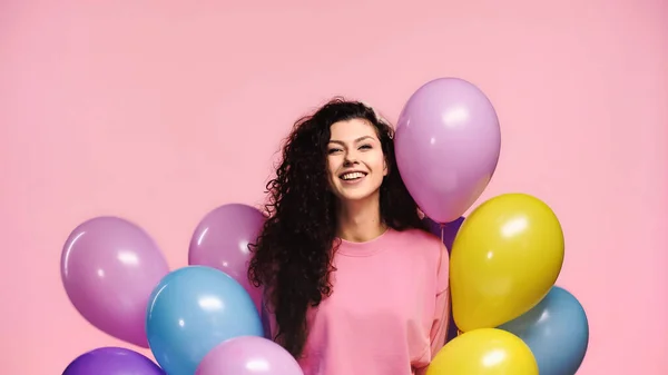 Mujer feliz con globos multicolores sonriendo a la cámara aislada en rosa - foto de stock