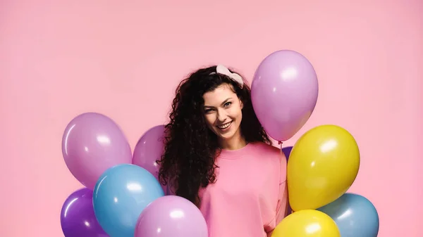 Веселая женщина с красочными воздушными шарами, смотрящая на камеру, изолированную на розовый — стоковое фото