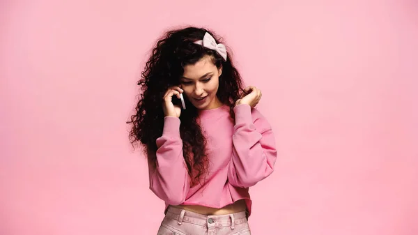Hübsche und positive Frau, die beim Telefonieren Haare berührt, isoliert auf rosa — Stockfoto