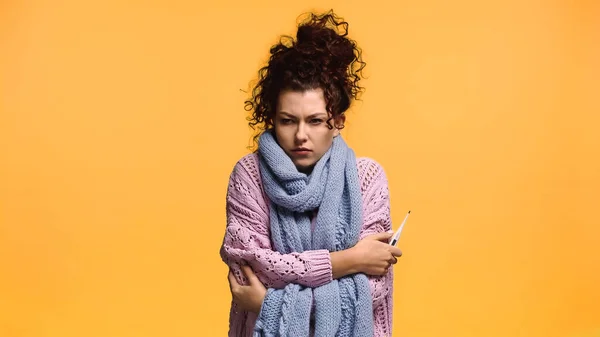 Mujer alterada y enferma en suéter de punto que sostiene el termómetro aislado en naranja - foto de stock