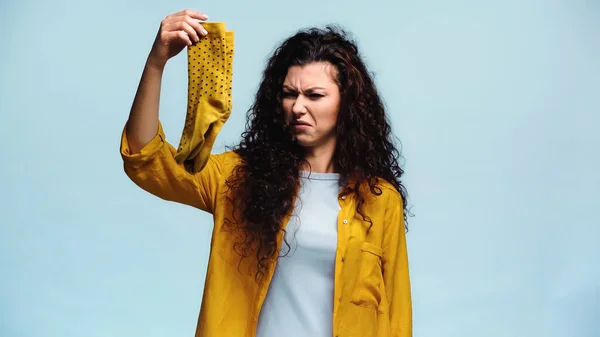 Mujer disgustada sosteniendo calcetines apestosos aislados en azul - foto de stock
