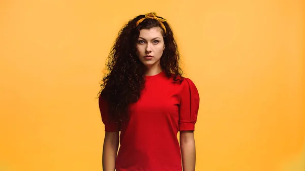 Mujer joven seria en blusa roja mirando la cámara aislada en naranja - foto de stock