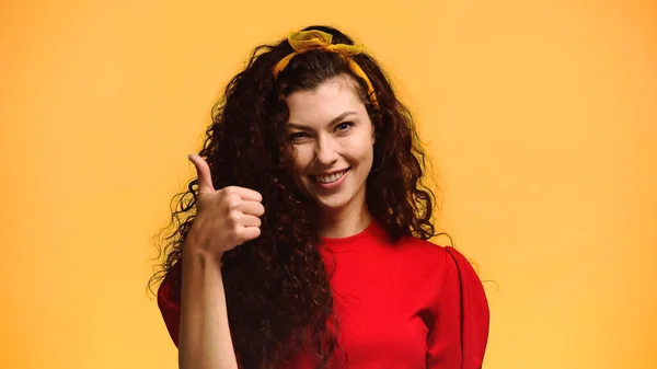 Happy brunette woman looking at camera and showing thumb up isolated on orange — Stock Photo