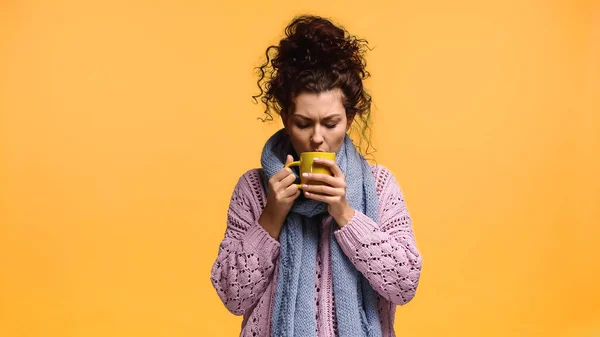 Mujer joven en suéter y bufanda bebiendo té caliente aislado en naranja — Stock Photo