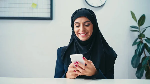 Feliz mujer de negocios musulmana utilizando el teléfono inteligente en la oficina - foto de stock