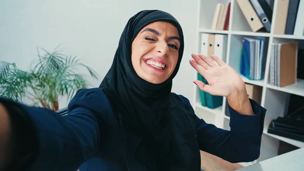 Smiling muslim businesswoman waving hand while taking selfie — Stock Photo
