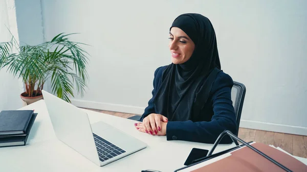 Mulher de negócios muçulmana alegre olhando para laptop no escritório — Fotografia de Stock