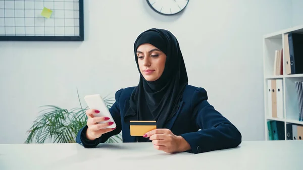 Mujer musulmana usando teléfono inteligente y tarjeta de crédito mientras hace compras en línea - foto de stock