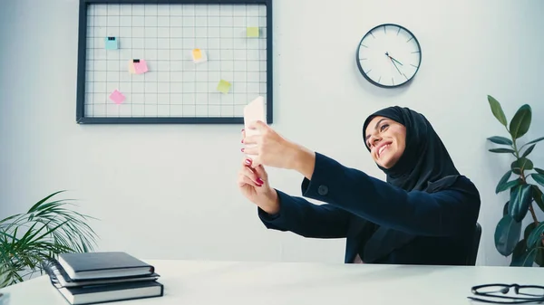 Feliz musulmana mujer de negocios tomando selfie en el teléfono inteligente en la oficina - foto de stock