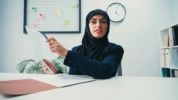 Мусульманська жінка в хіджабі вказує ручкою на документ в сучасному офісі — стокове фото