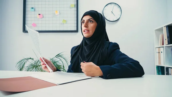 Mujer de negocios musulmana en hijab celebración de documento y pluma en la oficina moderna - foto de stock