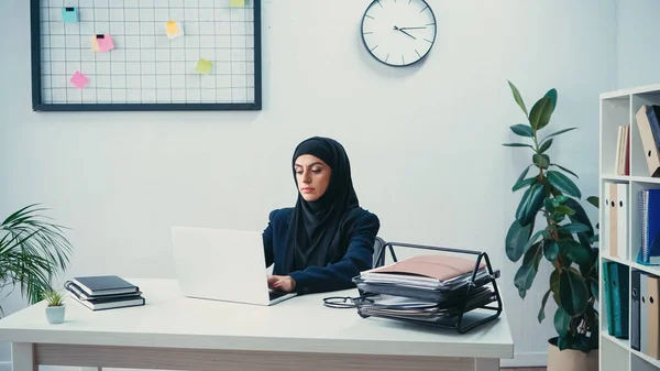 Мусульманская бизнесвумен в хиджабе печатает на ноутбуке в современном офисе — стоковое фото