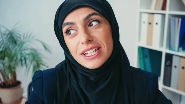 Joven mujer de negocios musulmana en hijab hablando mientras mira hacia otro lado - foto de stock