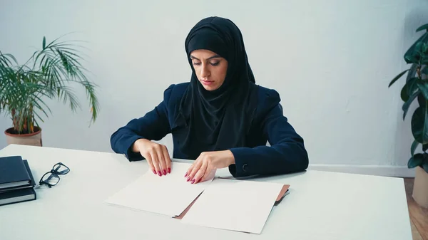 Молода мусульманка дивиться на документи на столі — стокове фото