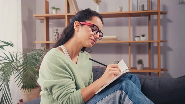 Estudiante morena escribiendo en el cuaderno en casa - foto de stock