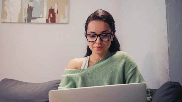 Freelancer in eyeglasses looking at blurred laptop at home — Stock Photo