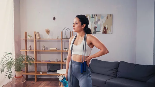 Sportswoman avec bouteille de sport et corde à sauter debout à la maison — Photo de stock