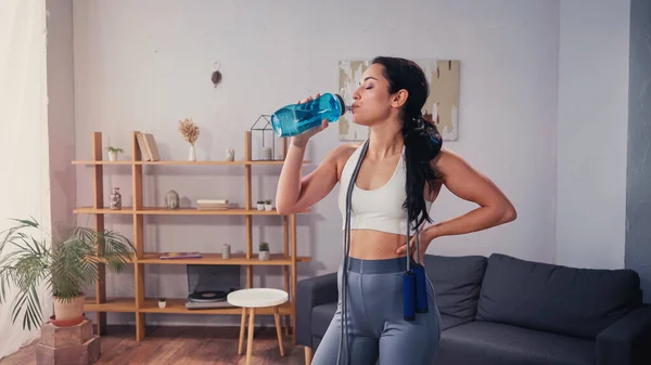 Side view of sportswoman with jump rope drinking water at home — Stock Photo