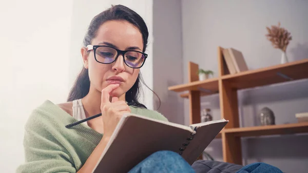 Estudiante enfocado sosteniendo cuaderno y pluma en casa - foto de stock