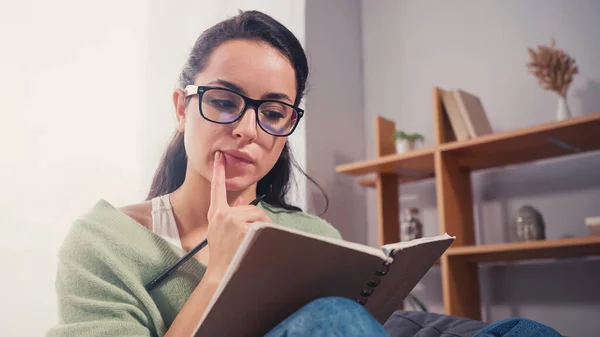 Nachdenklicher Student mit Brille schaut zu Hause auf Notizbuch — Stockfoto