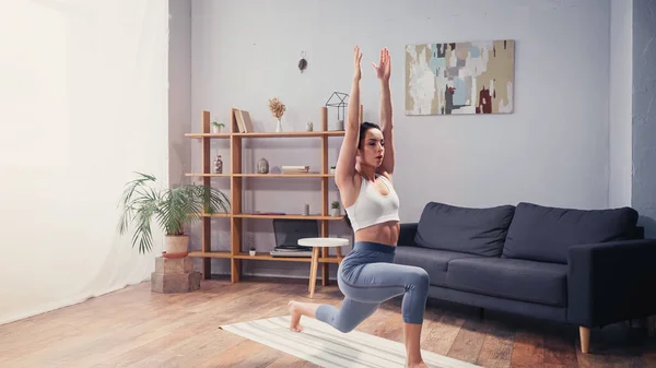 Sportlerin mit erhobenen Händen beim Ausfallschritt zu Hause — Stockfoto