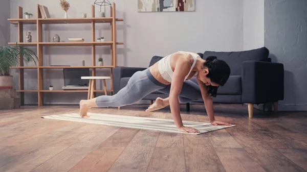 Mujer morena en ropa deportiva haciendo ejercicio en la alfombra de fitness en casa - foto de stock